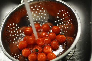 Washing Fresh Cherry Tomatoes in Metal Colander under Running Water in Kitchen Sink