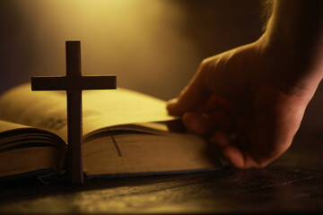Hand Turning Page of Bible with Wooden Cross Under Warm Light