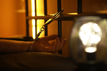 Dimly Lit Prison Cell with Handcuffed Hand Reaching Out from Behind Bars