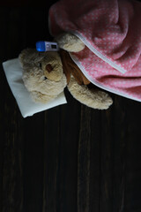 Sick Teddy Bear in Bed with Thermometer and Pink Blanket