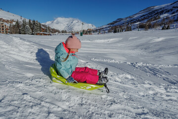 Little girl in pastel coat slides down on green sled, have fun