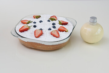 Tres Leches Cake in a clear glass baking dish topped with fluffy whipped cream garnished with vibrant fresh strawberry and blueberries side view of moist dessert