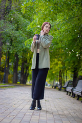 Fashion outdoor portrait of gorgeous long hair woman in green jacket with cup of coffe. Fashionable...