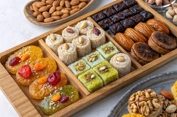 features a wooden tray filled with various types of traditional Middle Eastern sweets, nuts, and dried fruits. The sweets include colorful cookies, dates, and figs, all arranged neatly in compartments