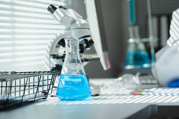 Blue chemical liquid inside an erlenmeyer flask on laboratory table with microscope and scientist working in background