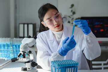 Scientist wearing lab coat and gloves analyzing blue liquid in test tube in laboratory