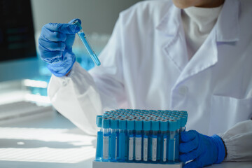 Scientist wearing lab coat and gloves analyzing blue liquid in test tube in laboratory with many...
