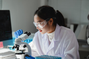Asian female scientist using a microscope in a laboratory, performing scientific research and...