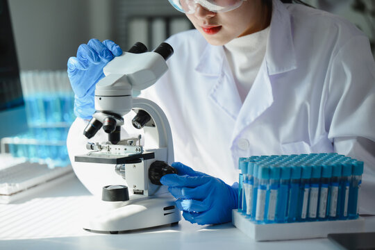 Scientist wearing lab coat and gloves adjusting microscope, conducting research in modern laboratory