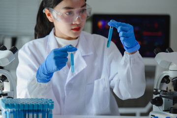 Scientist wearing lab coat and gloves comparing two test tubes with blue liquid in a laboratory
