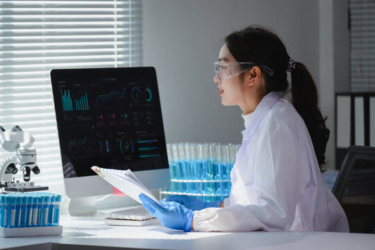 Scientist wearing lab coat and gloves analyzing data on computer in a modern laboratory with test tubes and microscope