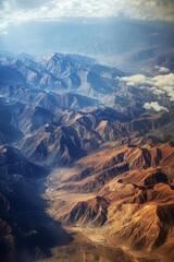 Aerial view of majestic mountain range with rugged peaks and valleys, showcasing dramatic textures and colors under soft clouds, capturing the beauty of nature's landscape