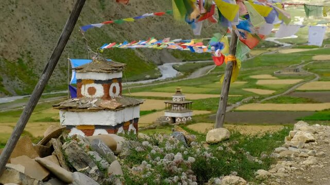 This breathtaking aerial drone footage captures a serene mountain valley featuring traditional Tibetan Buddhist stupas adorned with colorful prayer flags fluttering in the wind.