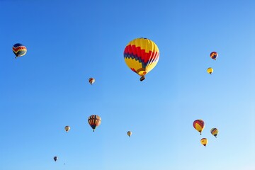 Obraz premium Skyward Spectacle: A fleet of colorful hot air balloons soars gracefully against a bright blue canvas, creating a breathtaking panorama. The scene conveys adventure and wonder. 