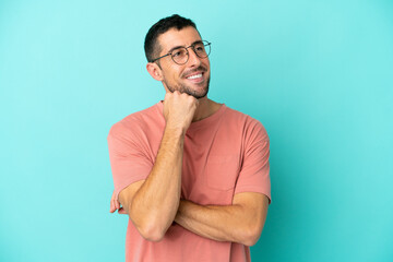 Young handsome caucasian man isolated on blue background With glasses and thinking while looking up