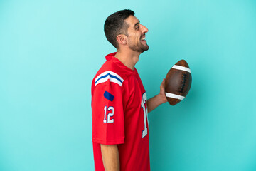 Young caucasian man playing rugby isolated on blue background laughing in lateral position