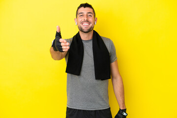 Young sport caucasian man isolated on yellow background shaking hands for closing a good deal