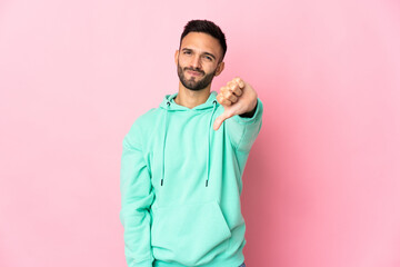 Young caucasian man isolated on pink background showing thumb down with negative expression