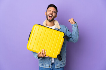 Young caucasian man isolated on blue background in vacation with travel suitcase