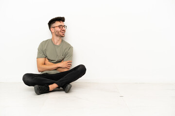 Young caucasian man sitting on the floor isolated on white background happy and smiling