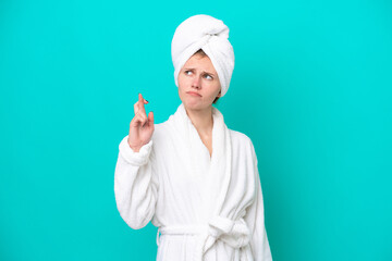 Young woman in a bathrobe isolated on blue background with fingers crossing and wishing the best