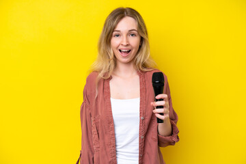 Young singer caucasian woman picking up a microphone isolated on yellow background with surprise...