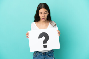 Young French woman isolated on blue background holding a placard with question mark symbol