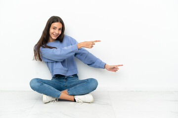 Young French girl sitting on the floor pointing finger to the side and presenting a product