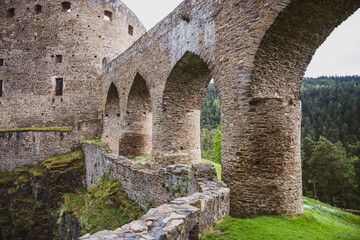 The Gothic bridge of Velhartice Castle stands majestically, surrounded by lush greenery. Its stone arches offer a glimpse into the historical architecture and scenic beauty of Czechia's landscape.