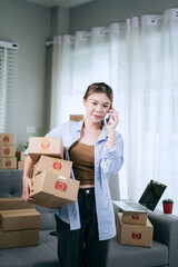 An Asian woman entrepreneur prepares parcels and manages her product orders via smartphone, ready to ship them to customers — reflecting the rise of online shopping and small business startups.
