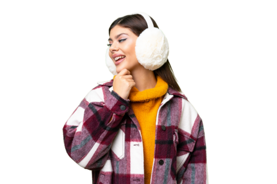 Young Russian woman wearing winter muffs over isolated chroma key background looking to the side