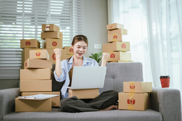 An Asian woman entrepreneur holds a coffee cup and her smartphone as she checks online orders and prepares packages for shipping — illustrating the spirit of modern SME startups and the growing trend 