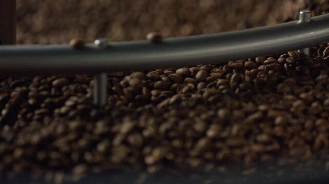 Professional coffee roasting machine mixing freshly roasted brown coffee beans during industrial production process in specialized workshop, showcasing detailed roasting technique