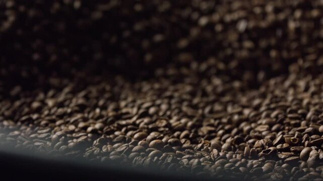 Professional coffee roasting equipment mixing freshly roasted coffee beans, revealing dark brown texture and rich roasting process inside industrial metal machine