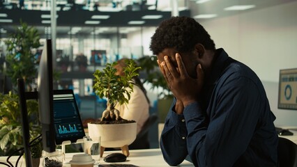 Overworked man having migraine symptoms while working on PC, drinking water to recover. Tired...