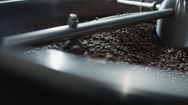 Industrial coffee roaster spinning freshly harvested coffee beans, distributing heat evenly and developing rich flavor profile during professional roasting process