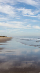Obraz premium Serene coastal beach with wet sand reflecting a beautiful sky and soft ocean waves, beach, coast, shore, ocean, water, waves, wet sand, reflection, sky, clouds, blue sky, horizon, scenic, landscape, n