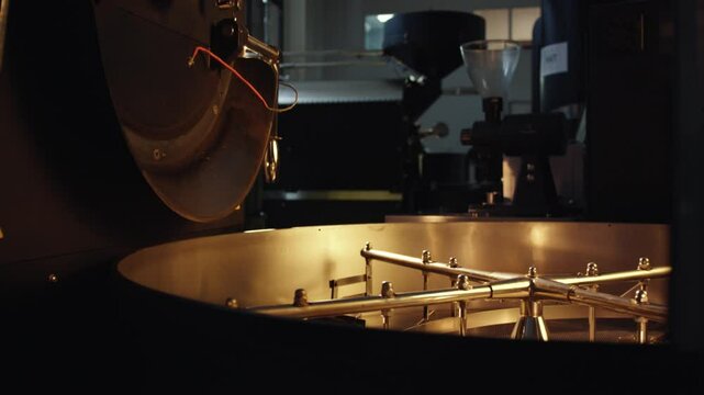 Professional coffee roasting machine with golden metallic arms systematically mixing and rotating coffee beans inside industrial workshop environment