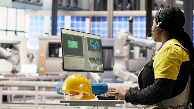 Automated manufacturing plant specialist analyzing live production data, using headset mic to communicate insights to engineers about robotic arms, conveyor belts and photovoltaic systems, camera B