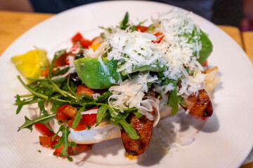 Delicious gourmet bruschetta topped with avocado, grilled sausage, arugula, and cheese. Captured on a restaurant plate for a fresh Italian culinary experience.