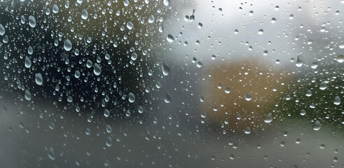 Fototapeta premium Rain droplets on a window with a blurred outdoor background, capturing a calm and moody atmosphere on a rainy day.