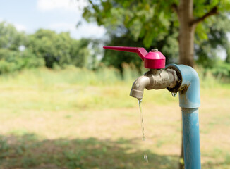 Outdoor water tap with a red handle dripping fresh water, symbolizing water conservation, drought, and the importance of saving natural resources in rural environments.