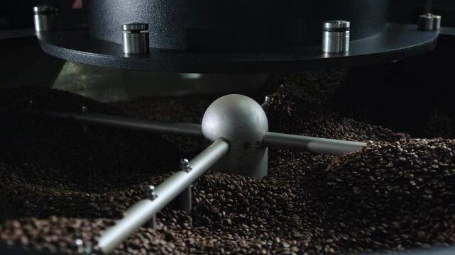 Professional coffee roasting machine rotating metal tool mixing freshly roasted brown beans, revealing detailed texture and aromatic transformation during industrial production process