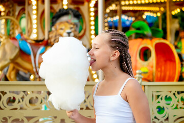 a child in an amusement and amusement park, a happy girl eating cotton candy and enjoying the...
