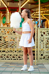 Fototapeta premium a child in an amusement and amusement park, a happy girl eating cotton candy and enjoying the holidays and summer, a child came to ride on a carousel