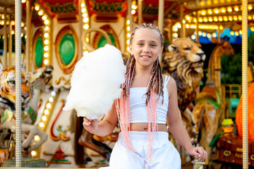 a child in an amusement and amusement park, a happy girl eating cotton candy and enjoying the...