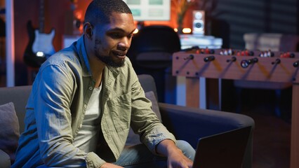 Focused African American guy teleworking on his laptop in a stylish living room. Remote worker...