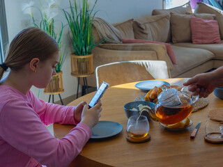 Relaxed tea moment with teapot and smartphone on wooden table. Bright natural light and cozy atmosphere in modern living room