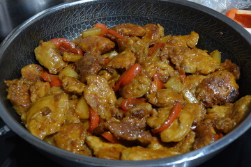 A close-up view of vibrant Chinese sweet and sour fried pork with red bell peppers in a dark pan.