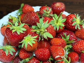 Ripe strawberries with green stems arranged on a white plate. Close-up shot highlighting fresh...